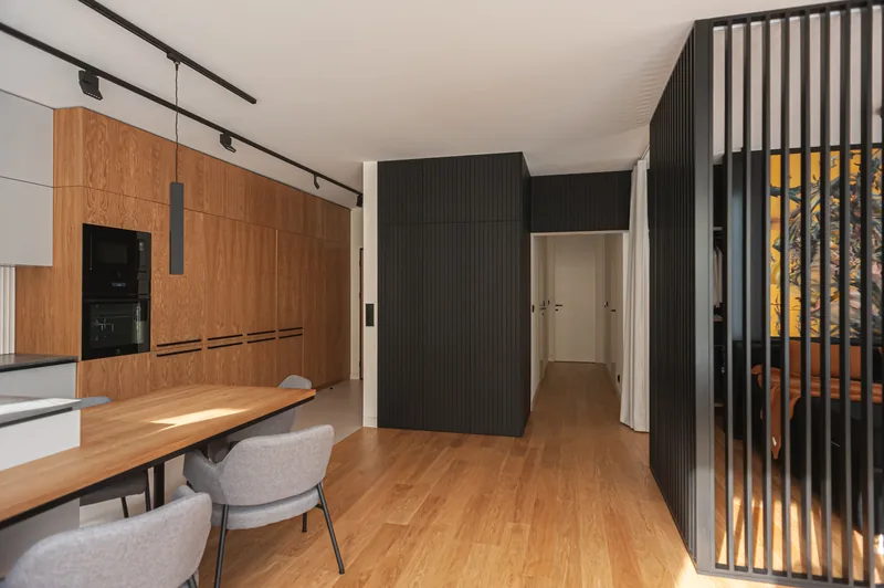 Apartament w Warszawie: kuchnia, drewniana podłoga i ciemna, frezowana zabudowa.